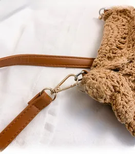 Detailed macro view of golden metal clasp and brown faux leather strap on woven bag