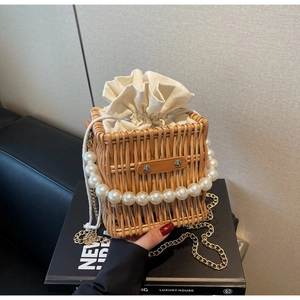 Close-up of woven straw bucket bag featuring a luxury pearl handle and gold chain strap