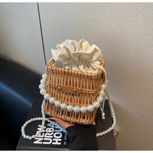 Detail of woven straw handbag featuring elegant pearl bead handles and drawstring canvas liner