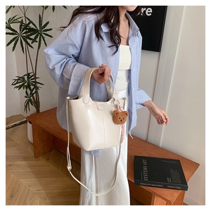 Bolso tipo cubo beige con amuleto de oso de peluche en un entorno de estilo de vida