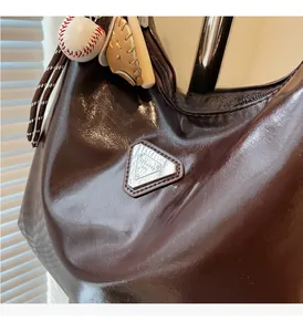 Close-up of a glossy brown hobo bag with a triangle logo and baseball glove charm