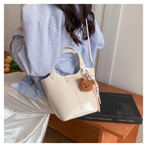 Elegante bolso bombonera de cuero crema con colgante de oso usado como bandolera