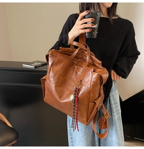 Close-up of a brown vintage leather backpack with stylish tassel charm detail in a cafe setting