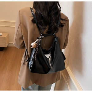 Close-up of black polished faux leather tote bag with silver triangle plaque and charm