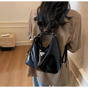 Detail shot of a black glossy backpack with triangle logo and cute bear charm on a model