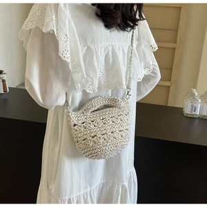 Detail der weißen Häkel-Eimertasche mit Webriemen auf einem weißen Spitzenkleid