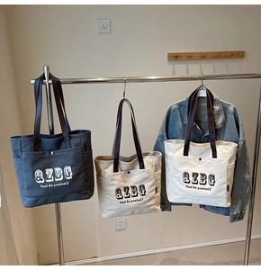 Dettaglio di borse tote in tela in tre colori con manici in pelle e scritte stampate