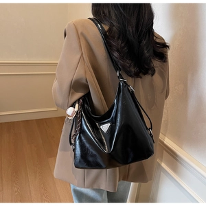 Detail of glossy black hobo tote with metallic logo and baseball charm accessory