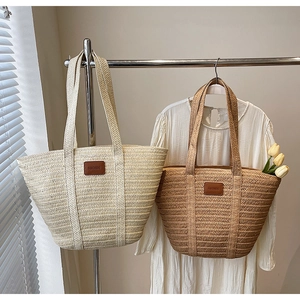 Detail of hand-woven straw tote bags in cream and tan with leather logo patch for summer