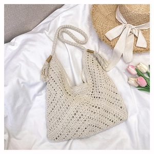 Flat lay of handwoven straw tote with tassels, summer hat, and tulips on white fabric