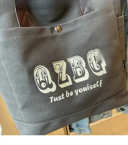 Dettaglio della borsa tote in tela grigia con scritte grafiche bianche e tasca frontale