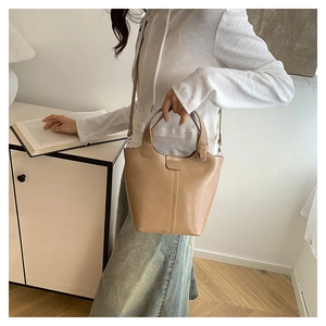 Detalle de bolso tipo cubo de cuero beige con costuras verticales y correa ajustable