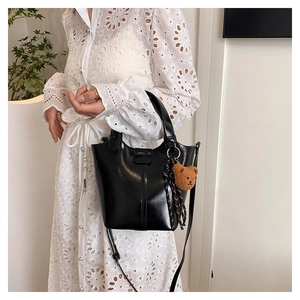 Detalle de bolso saco de cuero negro brillante con colgante de oso y cinta a rayas