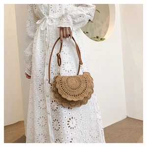 Close-up of bohemian woven straw bag with wavy edges on white lace dress background