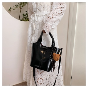 Detalle de bolso negro brillante con colgante de oso sobre un vestido blanco