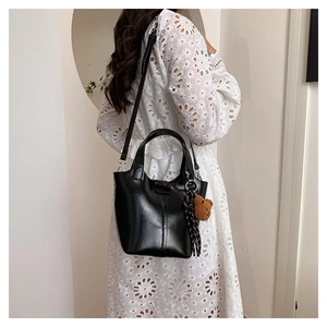 Detalle de bolso cubo negro brillante con colgante de osito y cinta elegante