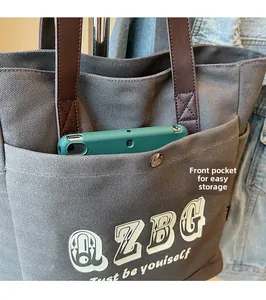 Dettaglio borsa tote in tela grigia con manici in pelle marrone e tasca frontale portaoggetti