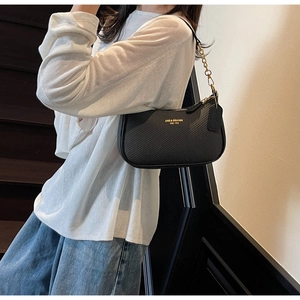 Detail of black textured leather handbag with gold chain strap and brand logo