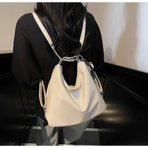Detail of cream versatile tote bag shown as a backpack on a model with metallic logo