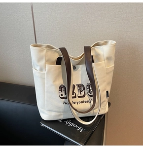 Dettaglio borsa shopper in tela con manici in pelle marrone e tasca laterale su divano