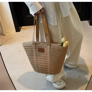 Detail of hand-woven straw tote bag with brown leather patch and floral accents