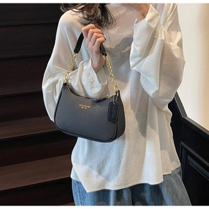 Close-up of black woven leather handbag with gold chain strap and brand embossing