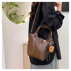 Bolso tipo cubo de cuero marrón con colgante de oso y correa tejida sobre modelo en negro