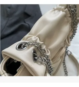 Close-up of pleated beige faux leather handbag featuring chunky silver chain details