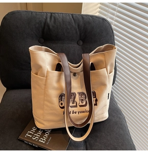 Dettaglio della borsa tote in tela con manici in pelle marrone e scritte artistiche