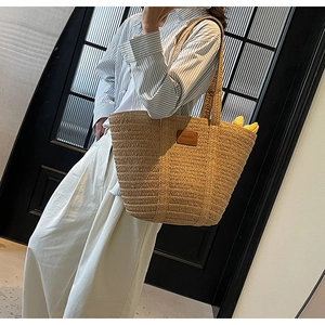 Detail of woven straw tote bag with brown leather patch and dual long shoulder straps