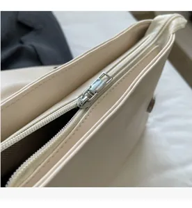 Detail view of smooth silver metal zipper and cream leather texture on the handbag
