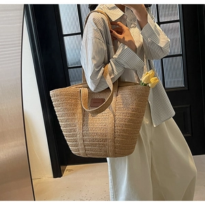 Detail of a beige woven straw tote bag with brown leather FASHION patch on shoulder