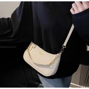 Close-up of cream woven texture handbag featuring gold chain and logo on black attire