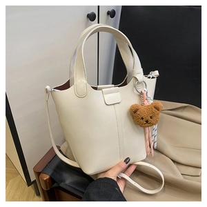 Detalle de bolso tipo cubo crema con asas y un adorable colgante de osito de peluche