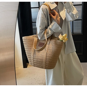 Detail of hand-woven straw tote bag featuring a brown leather patch and dual handles
