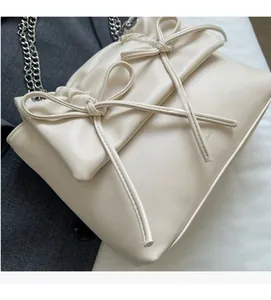 Detail of cream bow shoulder bag featuring silver chain strap and subtle logo embossing