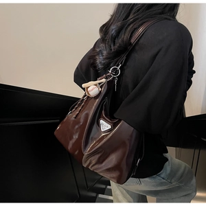 Detail of glossy brown tote bag with metallic triangle logo and baseball charm