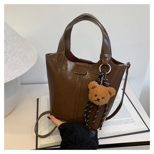 Detalle de bolso cubo marrón en cuero PU con colgante de oso de peluche y correa fina