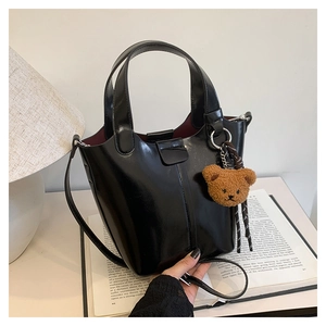 Detalle de bolso bucket de charol negro con colgante de oso de peluche sobre libro
