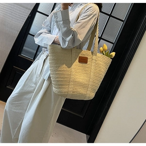 Detailed view of a large straw tote bag with a brown leather patch for beach or commute