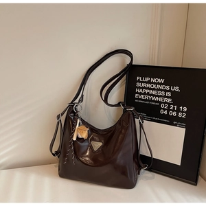 Detail of dark brown glossy leather tote bag with metallic logo and baseball charm