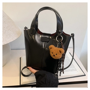 Detalle de bolso cubo negro brillante con colgante de oso de peluche en mesa blanca