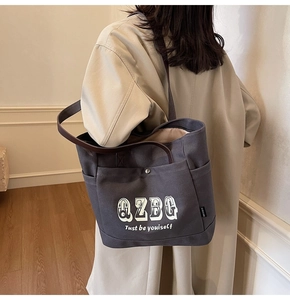 Dettaglio della borsa tote in tela con stampa QZBG e manico in pelle marrone su trench
