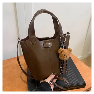 Detalle de bolso tipo cubo marrón oscuro con colgante de oso de peluche y piel granulada