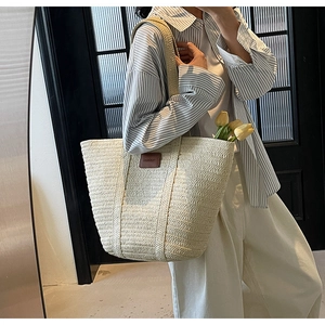 Close-up of handwoven beige straw tote bag featuring a premium brown leather logo patch