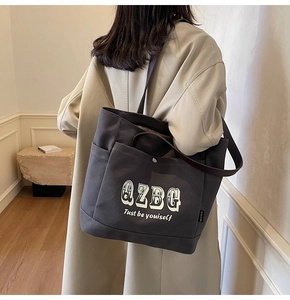 Dettaglio della borsa tote in tela grigio scuro con tracolla sopra un trench beige