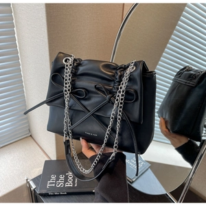 Detail of black pleated shoulder bag with bow accents and silver chain strap