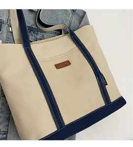 Detail of the cream canvas tote bag with dark blue webbing and a brown leather logo tag