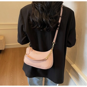 Detail of pink crescent bag with gold chain strap on model in black suit jacket