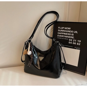 Detail of black glossy hobo bag with metal logo plate and baseball charm accessory